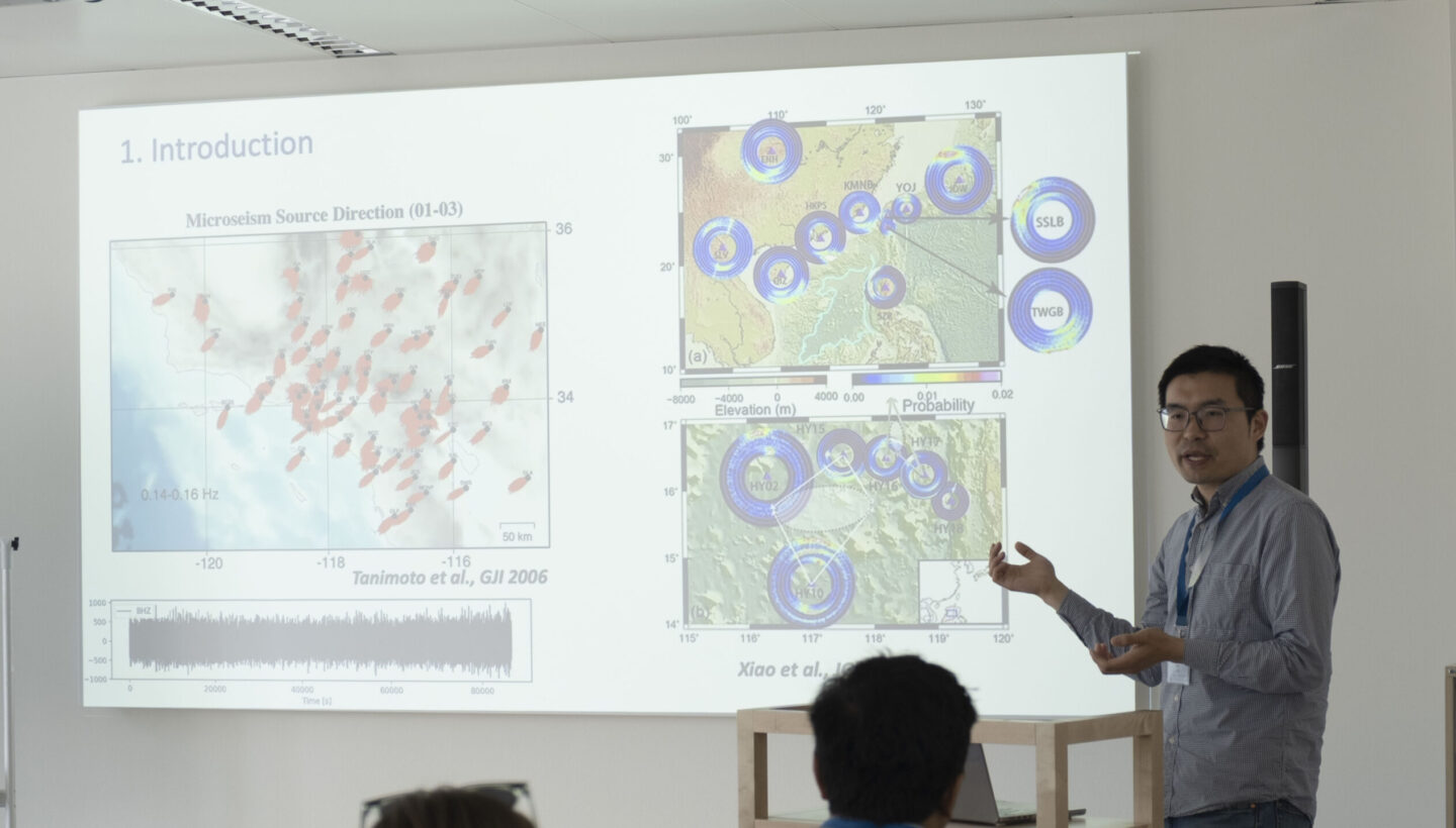 A presenter standing next to a projected slide. The slide shows different geographical weather data.