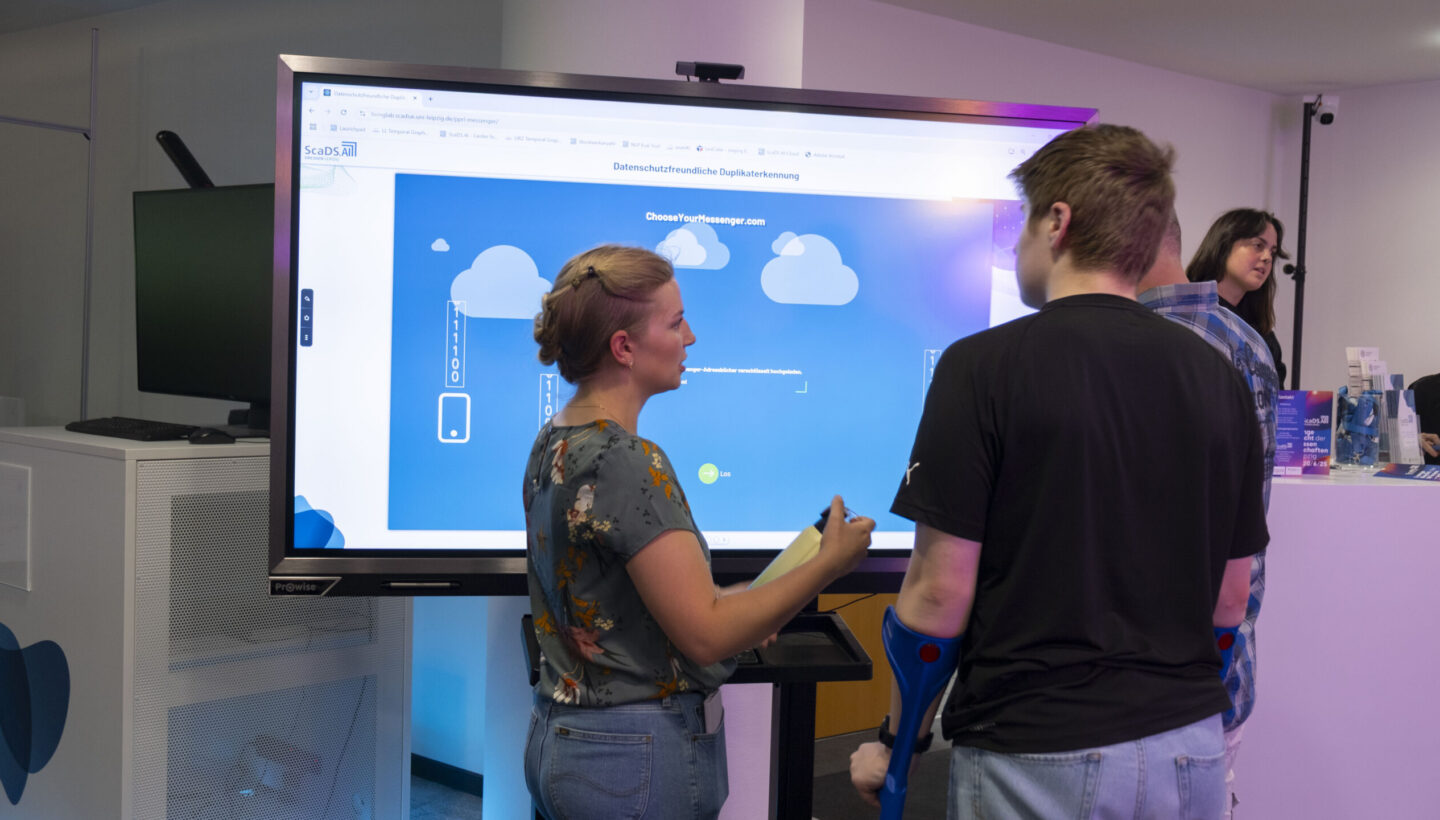 Photo. Visitors stand in front of a screen and talk.