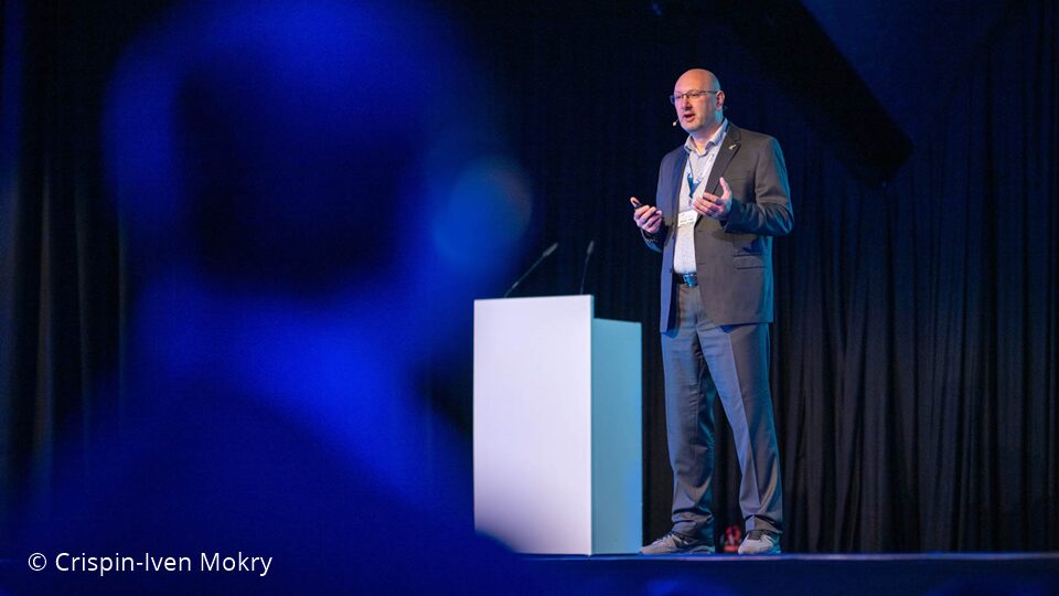 Photo. Christoph Kögler presenting at the All Hands Meeting of the German AI Community in 2024. © Crispin-Iven Mokry