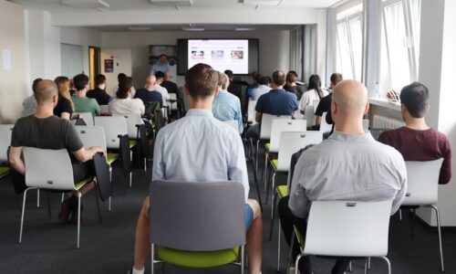 Photo. Julian Hagert is presenting in front of a large group of people at the first Meetup in Dresden.
