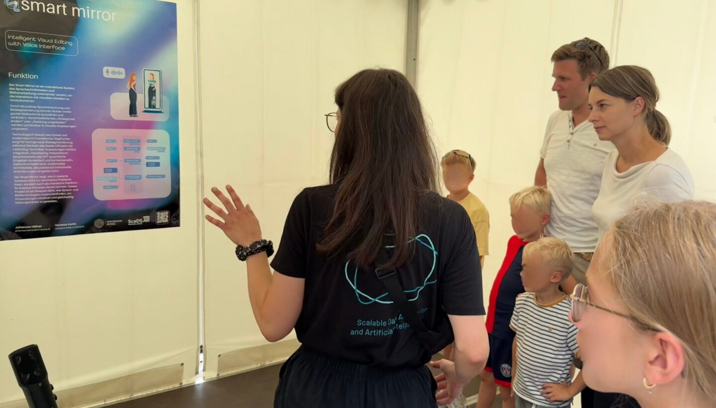 A presenter stands before a small audience next to a table holding a sleek device, explaining a large poster titled “smart mirror – Intelligent Visual Editing with Voice User Interface,” which outlines features such as image adjustment, adding effects, video editing, voice control, user-friendliness and powerful machine-learning-driven algorithms.