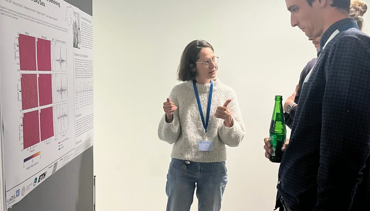 A person giving a short presentation next to a poster hung up on a partition wall.
