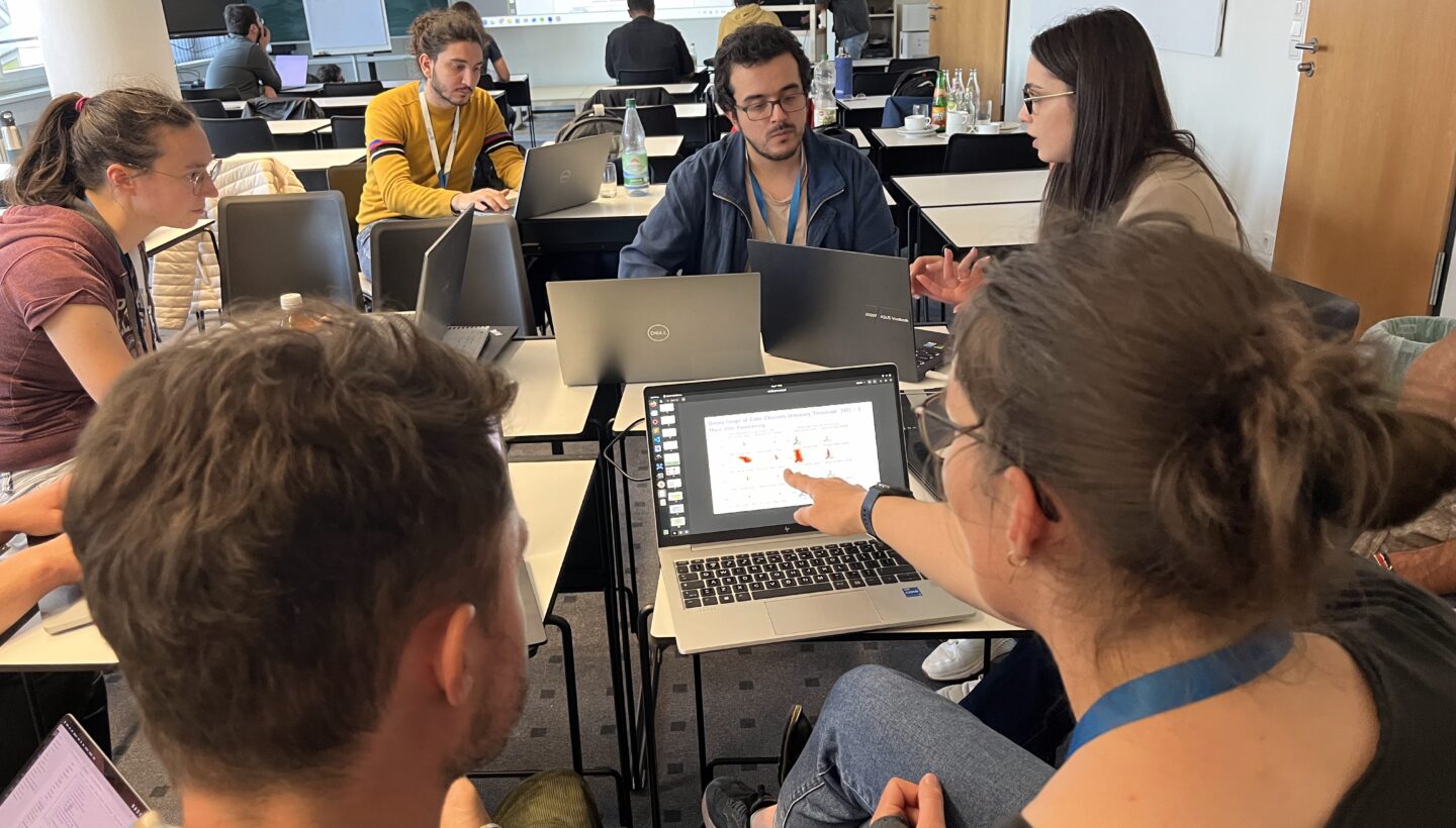 Five people sit around a conference-room table, each with an open laptop, attentively engaged in the "Bring your own Data" session at the Training School AI4 Seismology