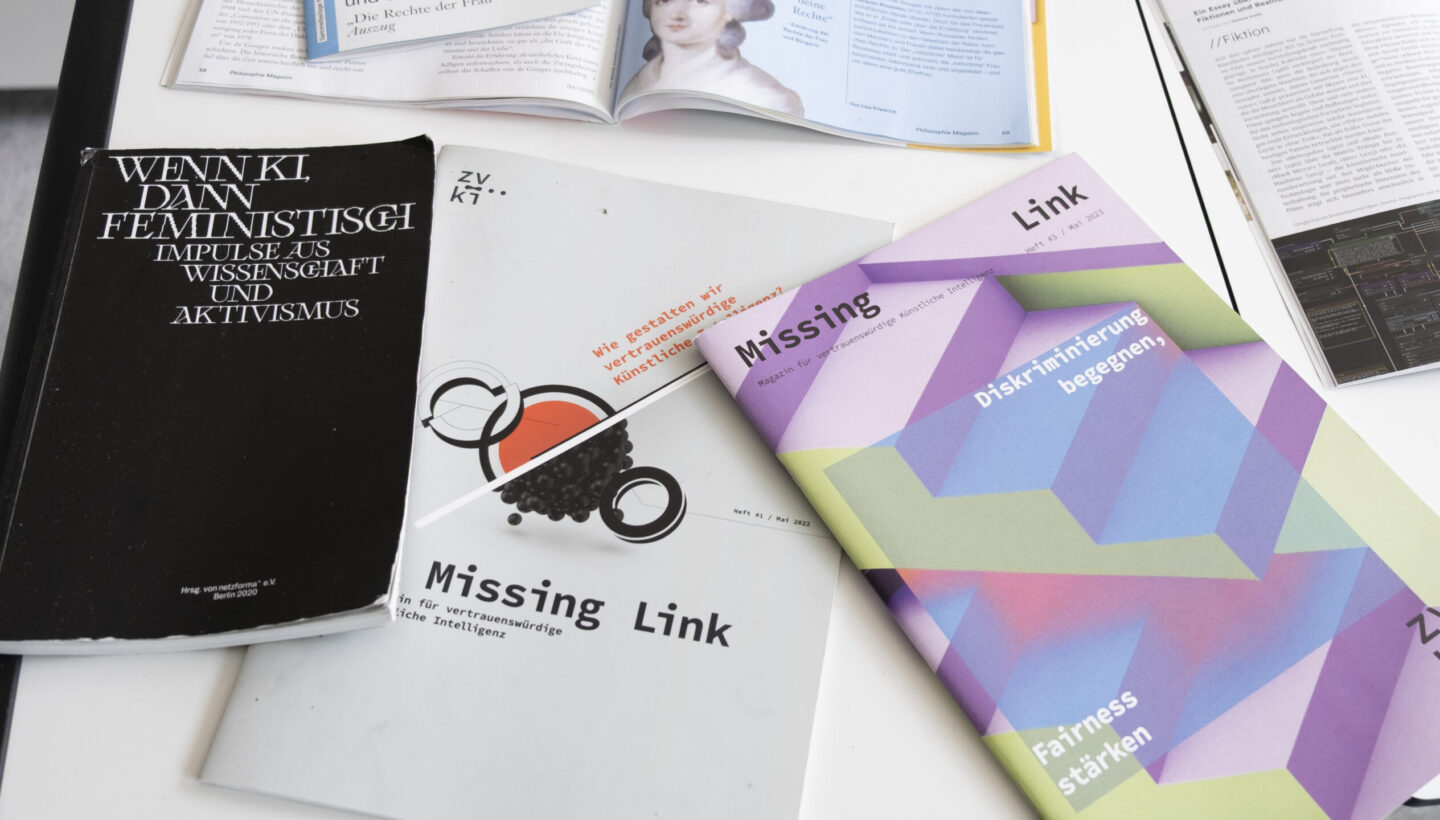 A close-up view of a literature table displaying a curated selection of books and magazines referenced during Vanessa Kuhfs’ presentation. The neatly arranged materials highlight the academic sources that informed the discussion at the KI Network Meeting.
