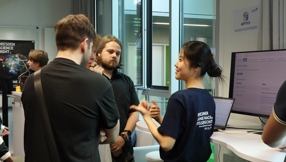 Photo. Yujia Hu is presenting the GPTKB demo to three visitors at the Living Lab in Dresden.