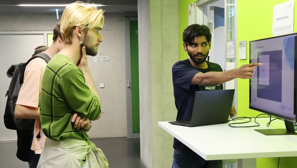 Photo. Lalith Manjunath is teaching two visitors the theoretical background behind the Maze Runner demonstrator at Lange Nacht der Wissenschaften 2025 in Dresden.