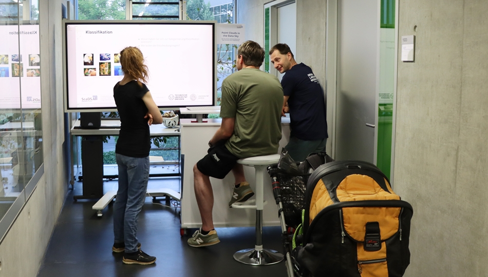 Photo. Dr. Christoph Lehmann is talking to two visitors of Lange Nacht der Wissenschaften 2025 about his demo "Punktwolken am Datenhimmel" in Dresden.