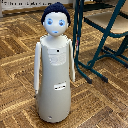 Photo. The AI-supported robot Navel is standing in a classroom, wearing a beanie. © Hermann Diebel-Fischer