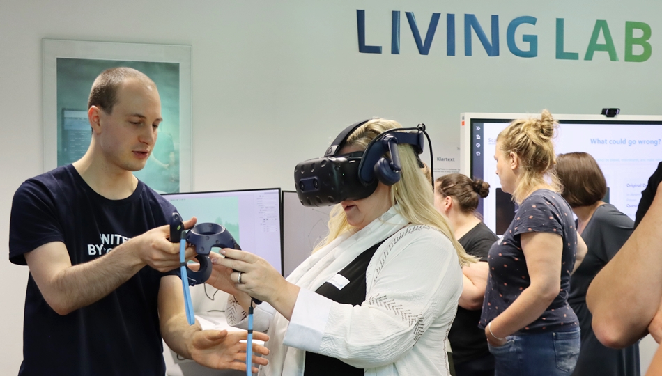 Photo. Moritz Müller explaining the FloodVis demo to a woman. In the back, there are 3 women trying out another demonstrator at the Living Lab.