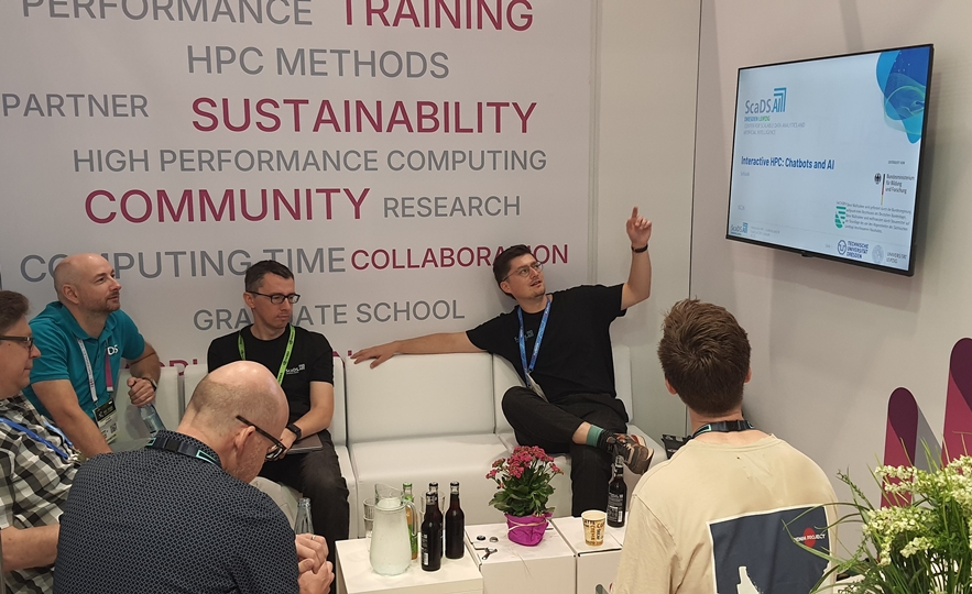 Photo. Elias Werner is giving the sofa talk "Interactive HPC: Chatbots and AI" at the booth of Verein für Nationales Hochleistungsrechnen (NHR).