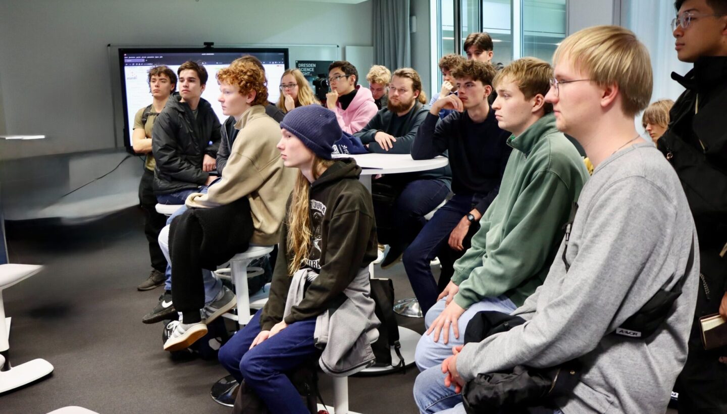 Photo. A group of students, are seated and standing in a Living Lab, all looking attentively in the same direction, paying attention to the presentation that is out of frame.